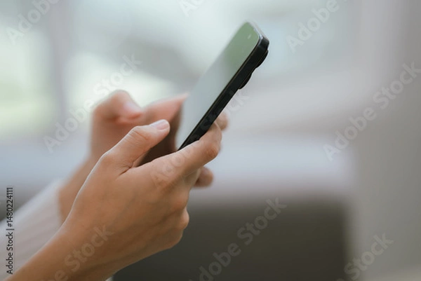 Fototapeta Close-up of a young woman's hand holding a smartphone and chatting on social media.