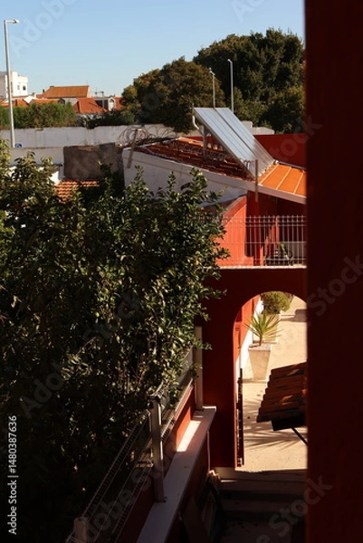 Obraz Urban residential scene featuring a rooftop solar panel and sunlit inner courtyard with red and white architectural elements.