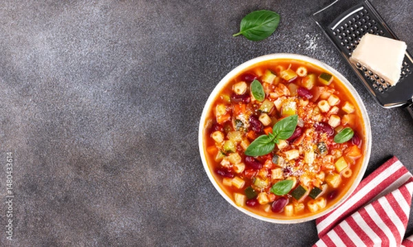 Obraz Italian minestrone soup with fresh vegetables, pasta, parmesan cheese on dark grey background. Top view. Copy space.