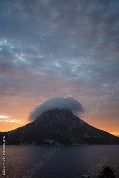 Fototapeta Scenic view of a cloud rolling around and over the mountain on Telendos island in Greece at sunset.