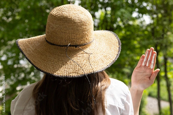 Fototapeta Closeup of a woman in a hat applying sufficient amount of sunscreen for the face and neck – three finger lengths.