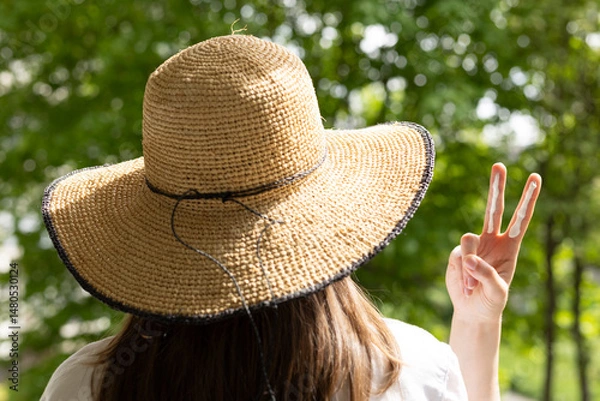 Fototapeta Closeup of a woman in a hat applying sufficient amount of sunscreen for the face and neck – two finger lengths.