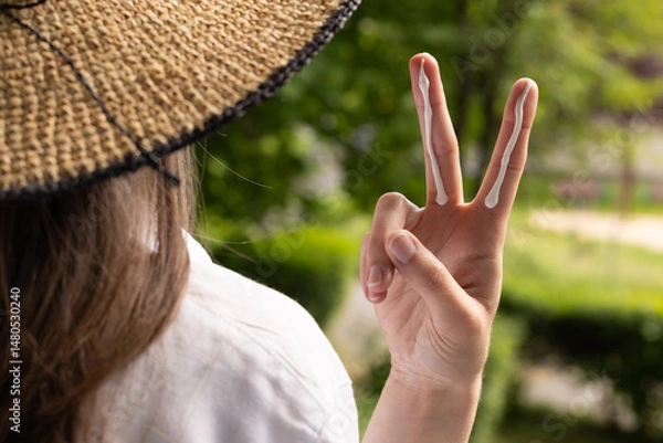 Fototapeta Closeup of a woman in a hat applying sufficient amount of sunscreen for the face and neck – two finger lengths.