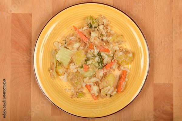 Fototapeta A top-down view shows a yellow plate with cooked carrots, cauliflower, and potatoes mixed with breadcrumbs on a wooden surface