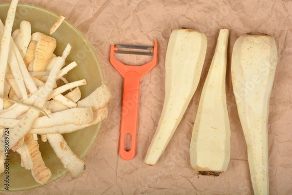 Fototapeta Peeled parsnips and their peels are arranged with an orange peeler on a brown paper background