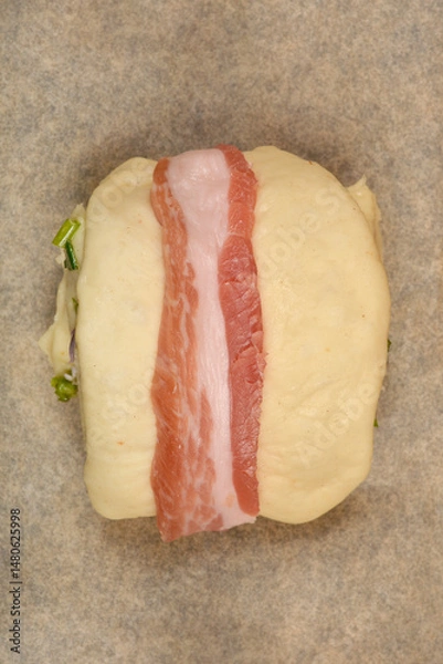 Fototapeta Bacon-wrapped dough rolls filled with a mixture of diced pancetta and herbs are arranged on a baking sheet, ready to be baked