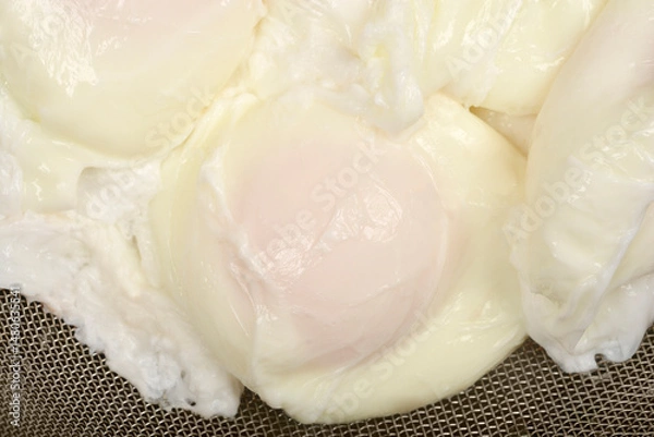 Fototapeta Poached eggsA close-up overhead shot shows several poached eggs with soft yolks and cooked whites resting in a metal sieve