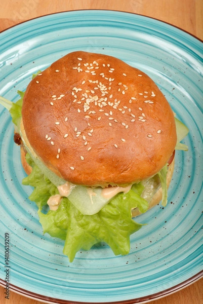 Fototapeta A delicious homemade burger with fresh lettuce and sauce is served on a light blue plate
