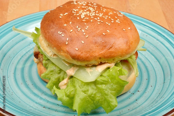 Fototapeta A delicious homemade burger with fresh lettuce and sauce is served on a light blue plate