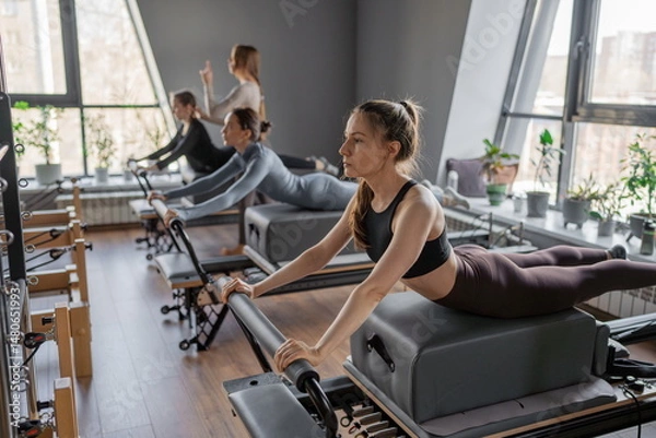 Fototapeta Womens doing Swan exercise on Pilates Reformer for the chest and back muscles, focusing on flexibility, strength, and control with determination