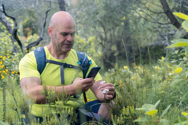 Obraz A hiker taking photos to wild flowers with the phone.