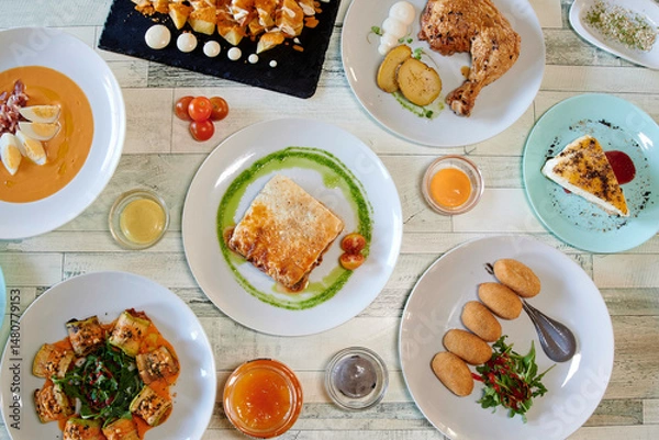 Fototapeta A table with many plates of food, including a plate of chicken. There are also bowls and spoons on the table