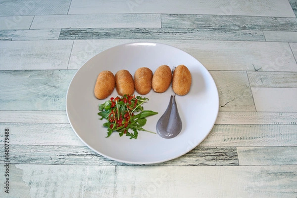 Obraz A plate of food with a spoon on it. The spoon is grey and has a greyish-blue color. The plate has a few pieces of food on it, including a few pieces of food that look like donuts