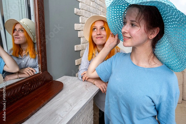 Obraz Two women are standing in front of a mirror, one wearing a blue hat