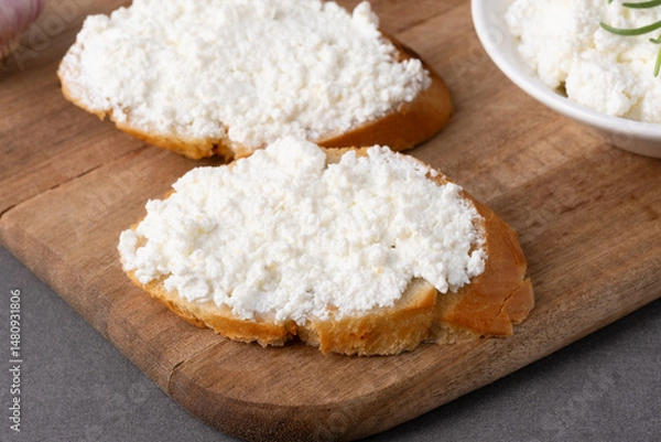 Fototapeta Slices of bread are spread with cream cheese and placed on a rustic wooden board.