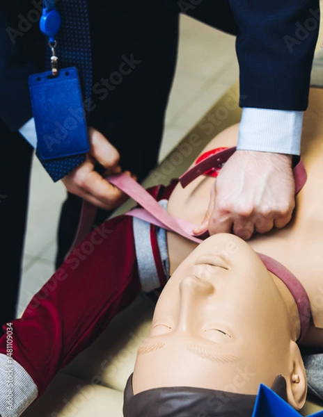 Fototapeta First aid training course with dummy, CPR emergency reanimation procedure on mannequin, instructor demonstrating medical training with doll, chest compression and applying bandage and tourniquet