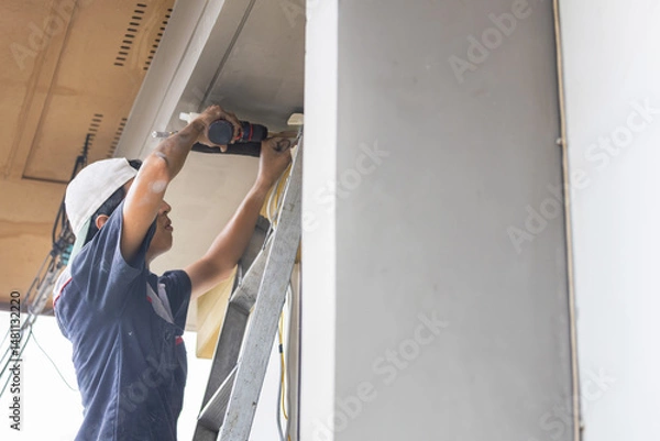 Fototapeta Air conditioning technicians install new air conditioners in homes, Worker using drill to install air conditioner