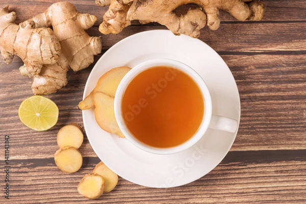 Fototapeta Cup of hot ginger tea and slices on wooden table. Top view
