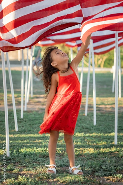 Obraz Smiling girl in red dress looking at American flag on Memorial Day, USA