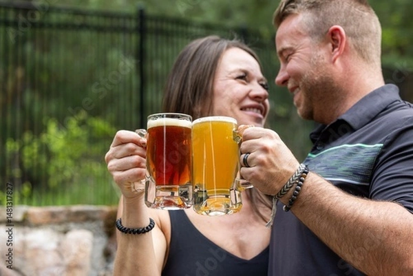 Obraz Couple celebrating and cheering with beer pints for National Beer Lover's Day.