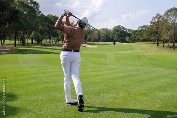 Fototapeta Professional female golfer lush green golf course, mid-swing after hitting a shot through after driving the ball down the fairway trees and distant sand bunkers, typical of a competitive setting.  