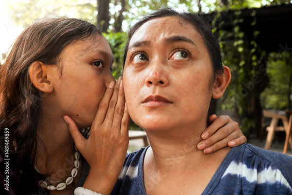 Fototapeta An Asian teenage girl whispering something to her mother's ear and her mother being a good listener. Intimate relationship between mom and daughter concept.