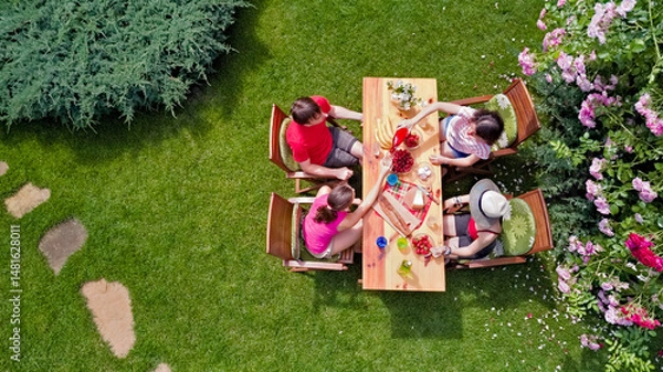 Fototapeta Family and friends eating together outdoors on summer garden party in park. Aerial view of table with food and drinks on grass from above. Leisure, holidays and picnic concept