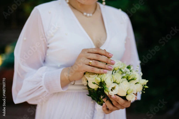 Obraz bride in a white trendy wedding dress holds a bouquet of white roses in her left hand and strokes the flower buds with her right hand, photo on an isolated background