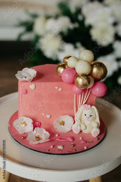 Obraz pink cake for celebrating a child's birthday, or a girl's birthday, the cake is decorated with white flowers, a toy bunny, and decorative balloons, the cake is on the table