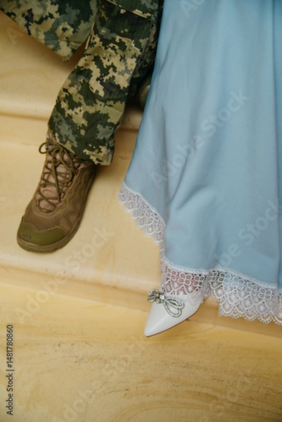 Obraz the feet of the bride and groom taking a step, the groom is dressed in a military uniform of the armed forces of Ukraine and the bride is dressed in a blue dress