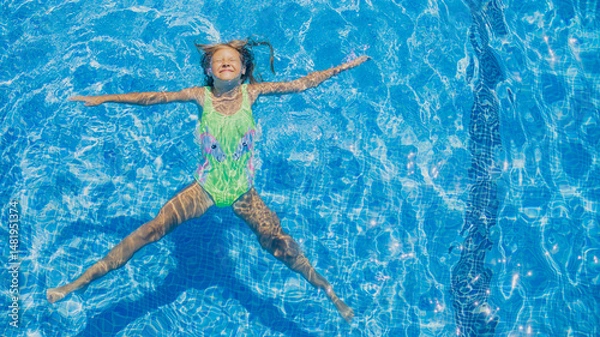 Fototapeta Young girl enjoys a joyful moment while floating in a bright blue swimming pool on a sunny day