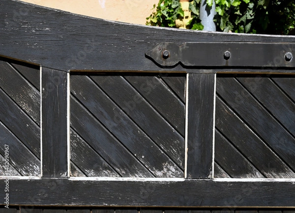 Fototapeta Weathered wooden gate in a rustic setting with shadows from surrounding foliage