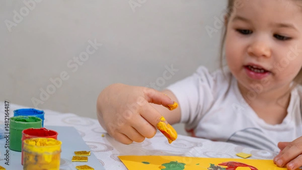 Fototapeta Happy smiling little girl enjoying creative finger painting activity, learning colors and shapes, improving fine motor skills through fun art and early childhood education.