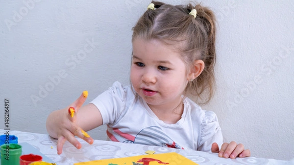 Fototapeta Happy smiling little girl enjoying creative finger painting activity, learning colors and shapes, improving fine motor skills through fun art and early childhood education.