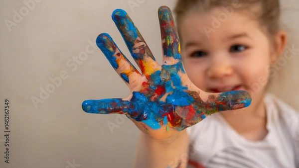 Fototapeta Little Girl Showing Hand Covered in Colorful Finger Paints, Smiling Playfully During Fun Creative Art Activity, Early Childhood Learning and Expression Concept