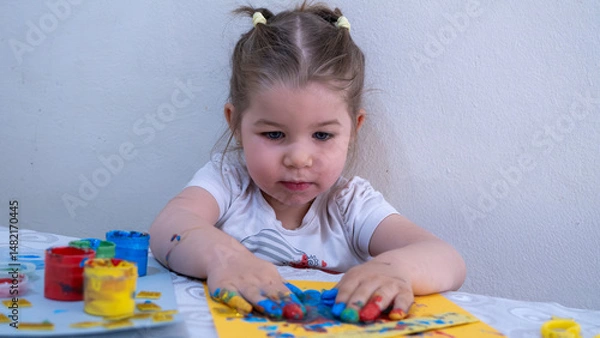 Fototapeta Concentrated Little Girl Creating Finger Paint Artwork, Hands Covered in Bright Colors, Focused on Artistic Expression and Fine Motor Skill Development in Early Childhood