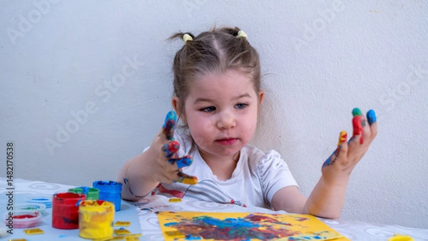Fototapeta Adorable Little Girl Joyfully Exploring Finger Painting with Bright Acrylic Colors, Showing Painted Hands and Creative Artworks, Fun Early Childhood Education Activity