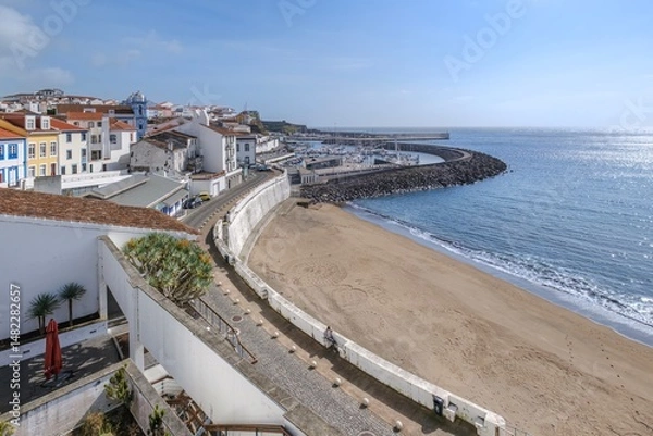 Fototapeta Sandy beach cove flanked by marina and mountain road on Terceira Island coastline. Aerial view of harbor entrance with shimmering Atlantic waters, stone breakwater and Mont Brasil hillside, Azores