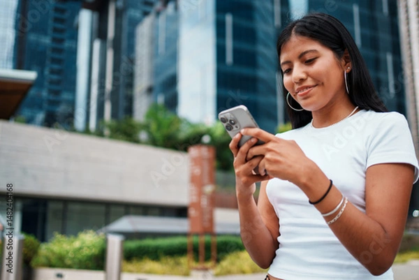 Obraz A young woman is using her smartphone while enjoying the urban city setting around her