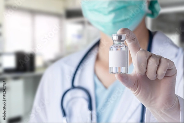 Fototapeta close up of glass bottle with blank white label for vaccine in doctor's gloved hand, blurry laboratory at background. concept of vaccine and medicine research for disease prevention at lab