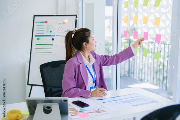 Obraz Happy attractive Asian businesswoman working on laptop and holding coffee cup with smile in Modern office or living room with copy space,E-commerce,internet technology, startup small business concept
