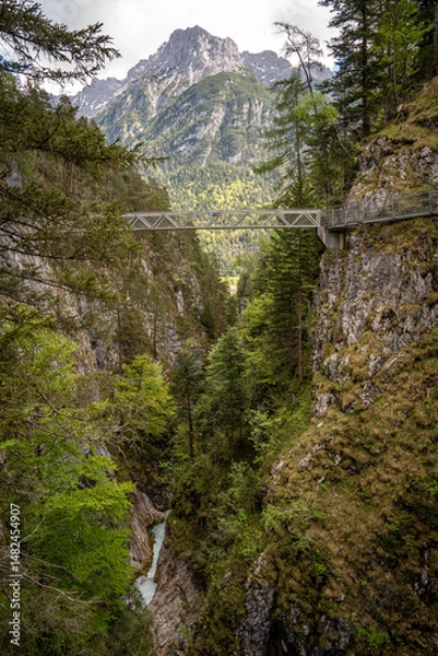 Fototapeta Spectacular View From Leutaschklamm Gorge: Elevated Steel Bridge Spanning Dramatic Rocky Cliffs Above A Narrow Waterfall-Fed Canyon Surrounded By Dense Alpine Forests With Karwendel Peaks In The Backg