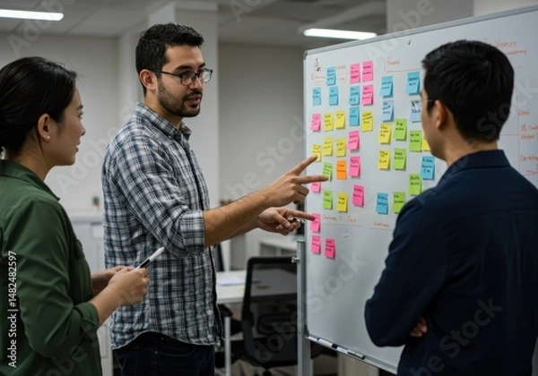 Fototapeta Three colleagues are discussing ideas using sticky notes on a whiteboard in the office