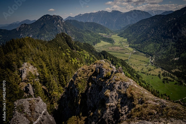 Fototapeta Breathtaking View From Naturpark Ammergauer Alpen: Dramatic Mountain Ridges, Lush Green Valley, And Rolling Hills Under A Clear Blue Sky In The Heart Of The Scenic Bavarian Landscape