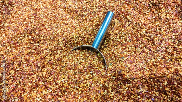 Fototapeta Red chilli hot peppers grounded clos up view in a container with metal scoop