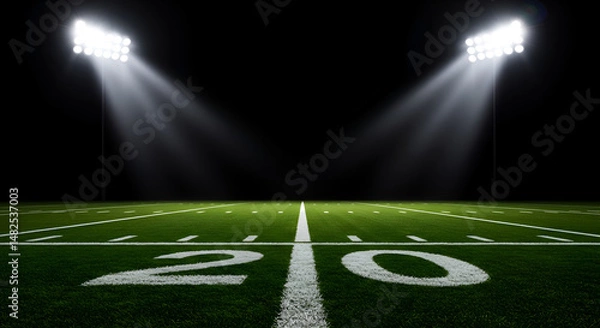 Fototapeta Dramatic view of an empty American football field's 20-yard line illuminated by bright stadium floodlights at night. Green turf ready for game day action. Perfect sports background.