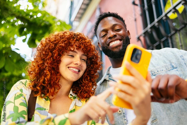 Fototapeta Two happy tourists are using a smartphone and smiling outdoors