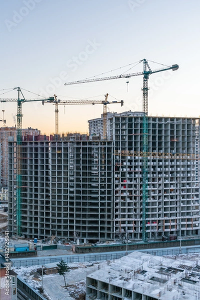 Fototapeta Construction site, cranes and multi-storey unfinished buildings at sunrise or sunset