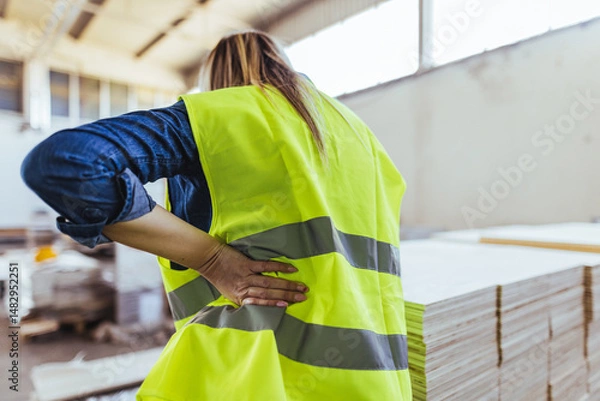Fototapeta Worker Experiencing Back Pain in a Construction Warehouse Environment