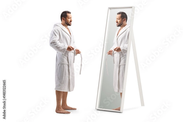Fototapeta Full length profile shot of a man putting on a bathrobe in front of a mirror